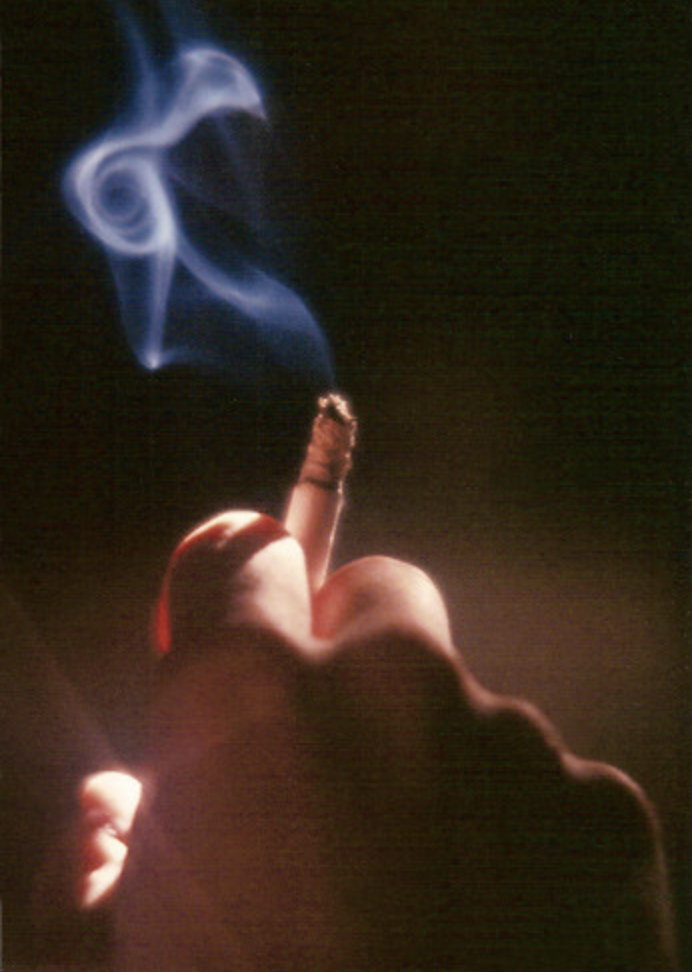 A hand holding a cigarette as smoke rolls out of it